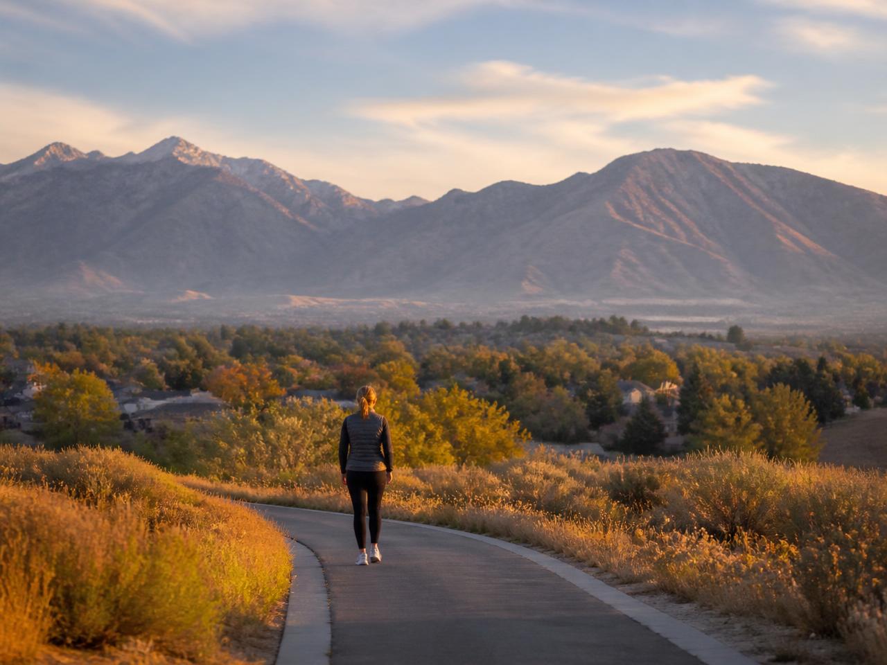 A person walking on a neighborhood trail at sunset with the Wasatch mountains behind them